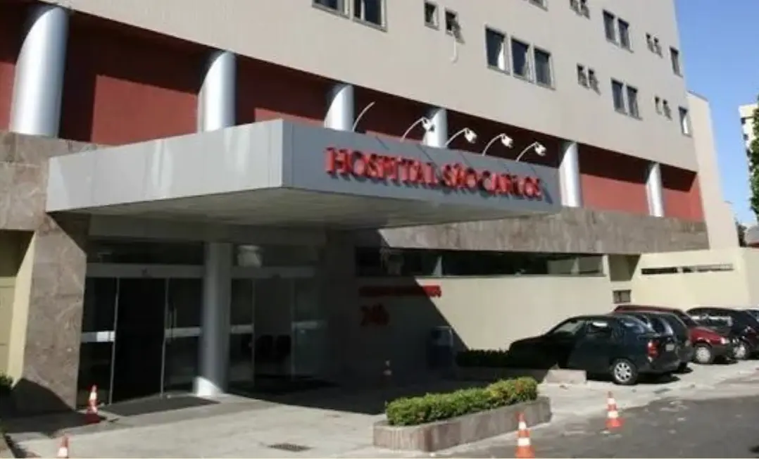 Fachada bege de um prédio com recuo e entrada avançada em cor metálica, escrito em vermelho de alto relevo Hospital São Carlos, se trata de uma unidade de internação hospitalar da rede referenciada Bradesco Saúde em Fortaleza