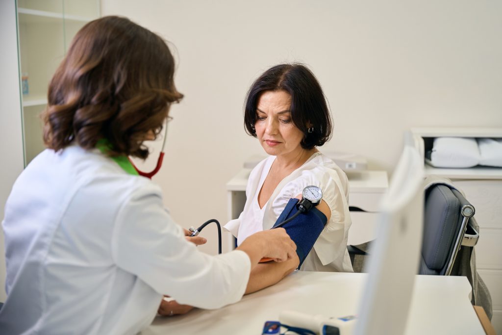 Médica realizando a aferição da pressão arterial de um paciente durante consulta de rotina, representando a importância dos check-ups regulares para a prevenção de doenças.