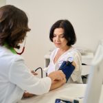 Médica realizando a aferição da pressão arterial de um paciente durante consulta de rotina, representando a importância dos check-ups regulares para a prevenção de doenças.