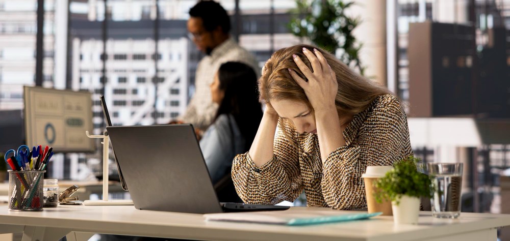 Pessoa sentada em uma cadeira, com a cabeça baixa, cobrindo o rosto com as mãos, demonstrando sinais de exaustão emocional e mental devido ao burnout.