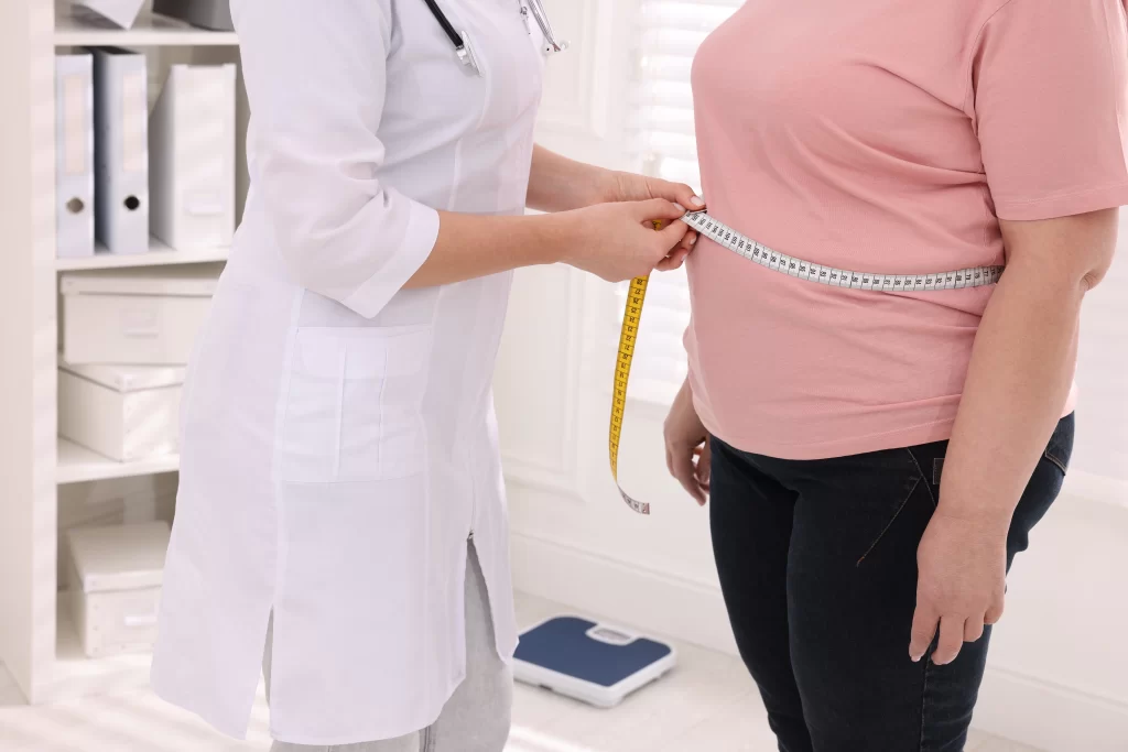 Nutricionista medindo a cintura de mulheres com excesso de peso em uma clínica, representando o acompanhamento oferecido por um plano de saúde para obesidade.