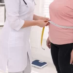 Nutricionista medindo a cintura de mulheres com excesso de peso em uma clínica, representando o acompanhamento oferecido por um plano de saúde para obesidade.